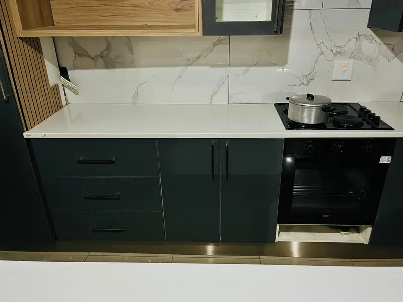 Charcoal base cabinets with a white worktop, built-in oven and a timber shelf above marble-effect tiles